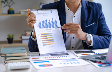 Business woman shows at graph on laptop and writing into notes or notebook.Computer screen with graphics and chart.
