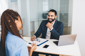 Cheerful Middle Eastern employer dressed in formal clothes listening information from blurred...