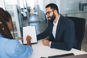 Middle Eastern male employee in classic spectacles for provide eyes protection talking with female colleague about financial report during business brainstorming cooperation in workspace, recruitment