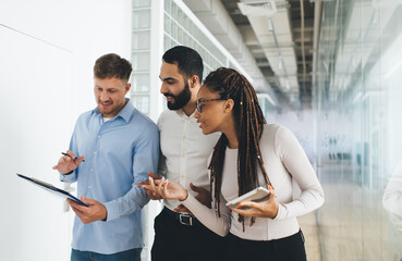 Professional male and female colleagues in smart casual wear talking about business statistics discussing office collaboration indoors, executive managers analyzing paperwork report in hallway
