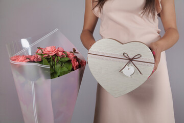 Young woman holding roses bouquet and gift box, gray color background.