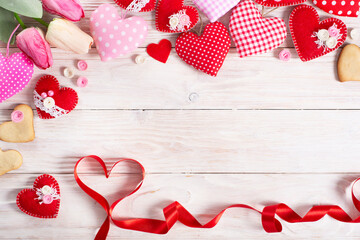 Sewed handmade fabric hearts tulips ribbon and cookies for valentine day on white wooden background with copy space