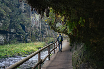 Rear view of adult man walking under sandstone rock formation in Bohemian Switzerland, Czech republic in autumn. Popular tourist destination and national park