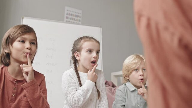 Medium slowmo shot of two boys and girl of elementary age doing articulation exercises with female speech therapist