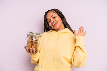 black afro woman smiling happily, waving hand, welcoming and greeting you. cookies concept