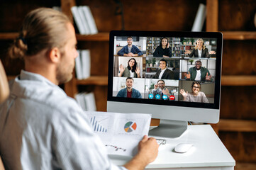 Online briefing, virtual business meeting. View over the shoulder of a company employee communicating with a group of multi-ethnic colleagues via video conference, analyzing financial statements