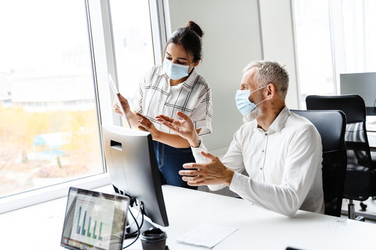 Multiracial colleagues in face masks talking during meeting at office