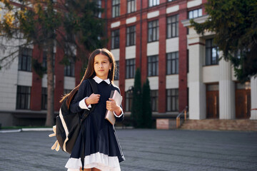 After lessons. Schoolgirl is outside near school building