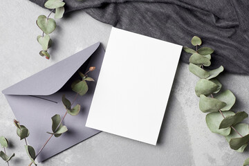 Invitation or greeting card mockup with envelope and natural eucalyptus twigs on grey concrete...