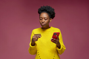 African american young girl holding credit card, phone, making payment, shopping. E-commerce,...