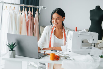 White colored sewing machine. Seamstress is in her office that is with different clothes