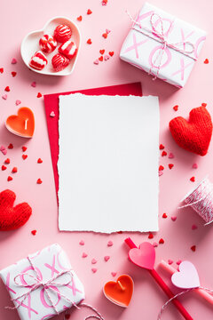Vertical Valentines Day background with blank paper card mockup, gifts, red hearts, confetti on pink.
