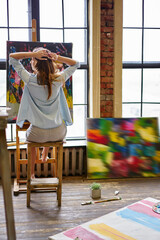 Talented Caucasian painter feeling freedom during art workshop in studio with canvas on easel, creating female artist with paintbrush spending weekend for drawing pictures and dye paintings