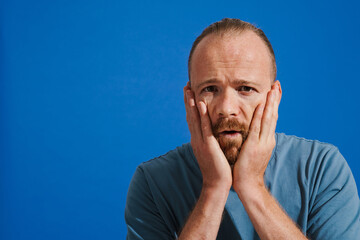 Ginger puzzled man holding his face while looking at camera