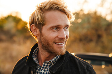 White man smiling while standing by car outdoors