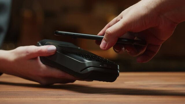 Paying with smartphone close-up. Cashless shopping in restaurant or cafe. Touch-free and contactless payment concept. NFC technology and bank terminal.