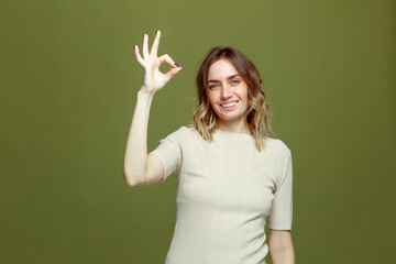 Fototapeta premium Smiling young woman show ok sign, making all right hand gesture on green studio background. Agreement, approval, confirm