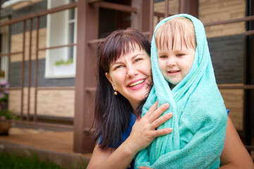 Mom hugs her little wet daughter in a towel outside after the rain. The concept of mother and daughter love
