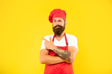 Winking man in toque and apron pointing finger aside yellow background, advertise
