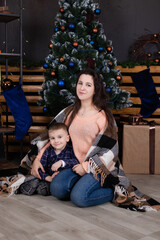 Fototapeta na wymiar Young mother in a beige knitted sweater near a Christmas tree with her son. single mother with child. family time. mothers love.