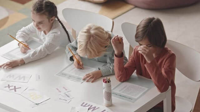 Top view slowmo shot of three Caucasian children of elementary age doing word search worksheet sitting at desk in classroom during speech therapy