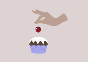 A hand putting a red sweet cherry on top of a muffin with a vanilla icing