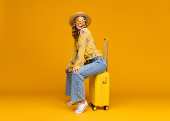 smiling woman traveling with suitcase dressed in trendy outfit on bright yellow background, positive summer vacation
