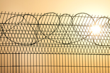 Barbed wire wall against the backdrop of the setting sun. Metaphor of slavery and the search for freedom