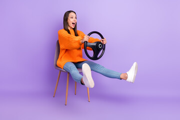 Profile photo of stunned lady hold steering wheel sit chair raise legs wear orange sweater isolated purple color background