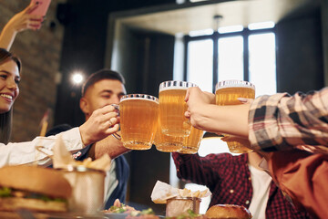 Cheering together. Group of young friends sitting in bar with beer