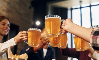 Cheering together. Group of young friends sitting in bar with beer