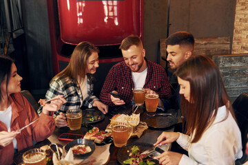 Women and men. Group of young friends sitting together in bar with beer