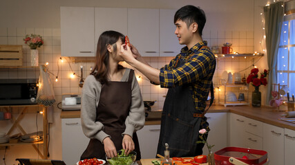 happy asian young couple having fun together playing with vegetable slices while preparing for...