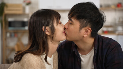closeup of asian romantic young couple gently kissing on lips at home. the woman looking at her boyfriend with a smile