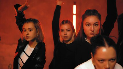 A group of beautiful girls dancing in a room with red lighting in black suits. Dances