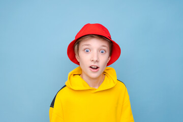 Portrait surprised young guy in yellow sweater and red panama hat on a blue background, looking at the camera with a smile on his face. Caucasian teenager posing in studio close-up studio portrait