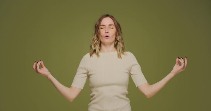 Young woman calming, breathing deep, meditating with mudra om gesture by hands, doing yogs exercise on green background