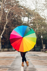 Vertical image of a modern woman showing her colorful umbrella to the camera. Impersonal photo of urban life on a windy and rainy winter day. Unrecognizable person.