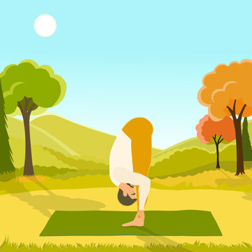 The young man performing Uttanasana pose or standing forward bend, working out outdoors on the autumn day in the beautiful park. 