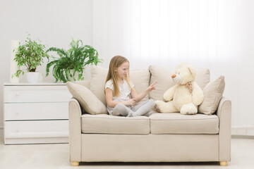 Photo of little girl in white clothes talking to teddy bear.