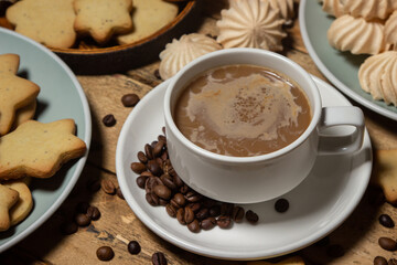 Cup of coffee on a wooden table. Coffee with milk, next to cookies and meringues. Coffee with dessert.