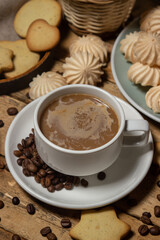 Cup of coffee on a wooden table. Coffee with milk, next to cookies and meringues. Coffee with dessert.