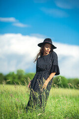 girl with hat on the meadow on the blue sky background with clouds