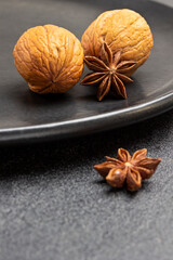 Two walnuts and star anise on edge of black plate.