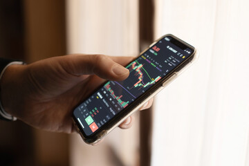 Investor working with smartphone, thinking and analyzing graph stock market trading with stock chart data planning, financial and investment concept. Closeup of hand
