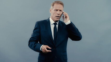Worried businessman talking on smartphone isolated on grey.