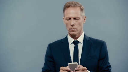 Mature businessman in suit chatting on smartphone isolated on grey.