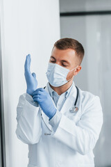 In blue gloves. Professional medic in white coat is in the clinic