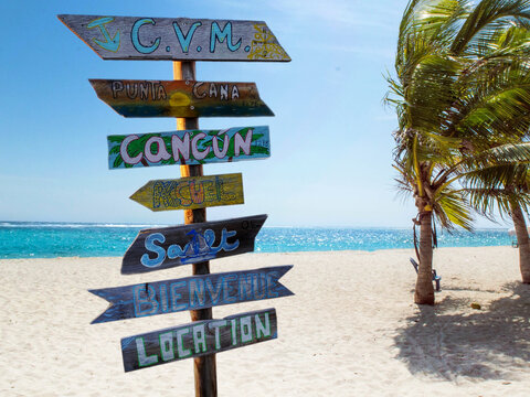 Street signpost on the beach indicating directions to different places of the world like Punta Cana in the Dominican Republic and Cancun in the Mexico