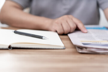 Close up pen on notebook and a man looking newspaper on the wood table